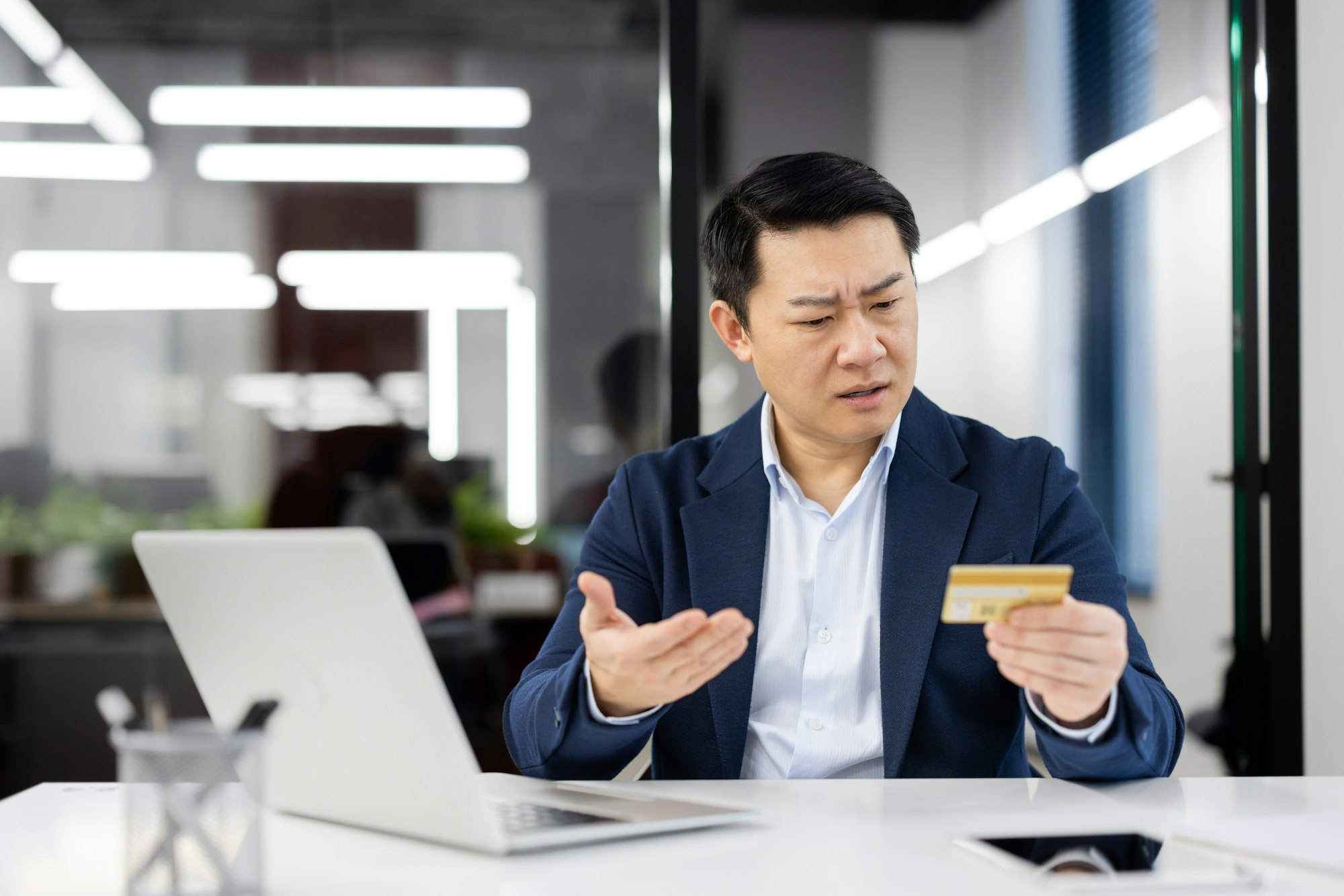 Businessman puzzled by credit card at modern office desk